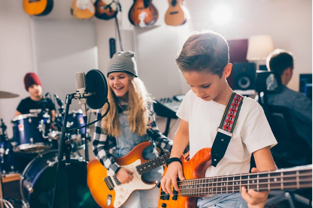 Children playing guitar, bass and drums together in a music studio
