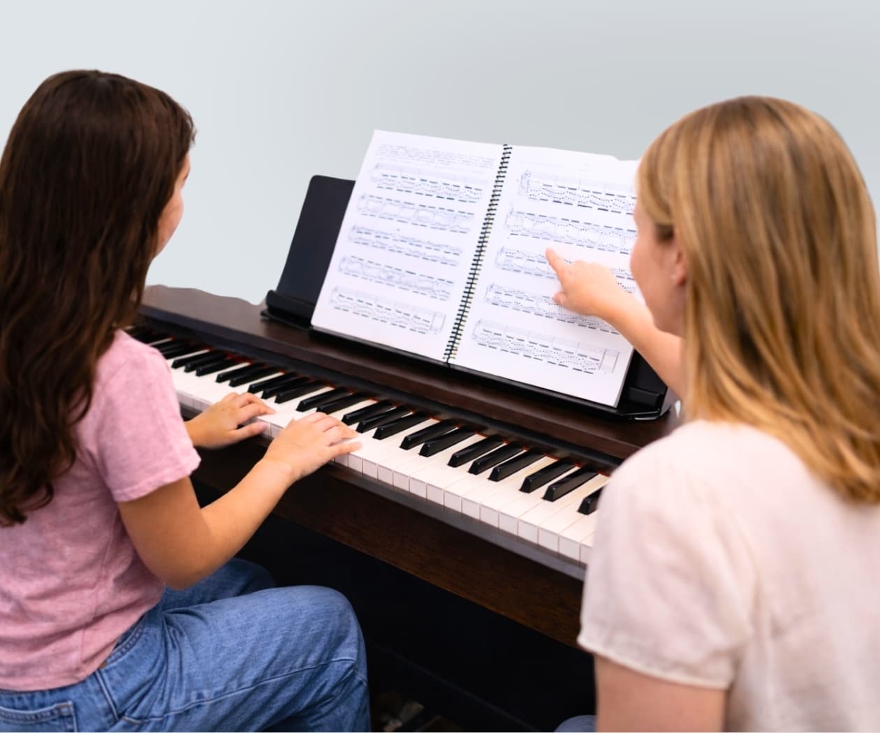 Piano teacher and student at a digital piano with sheet music
